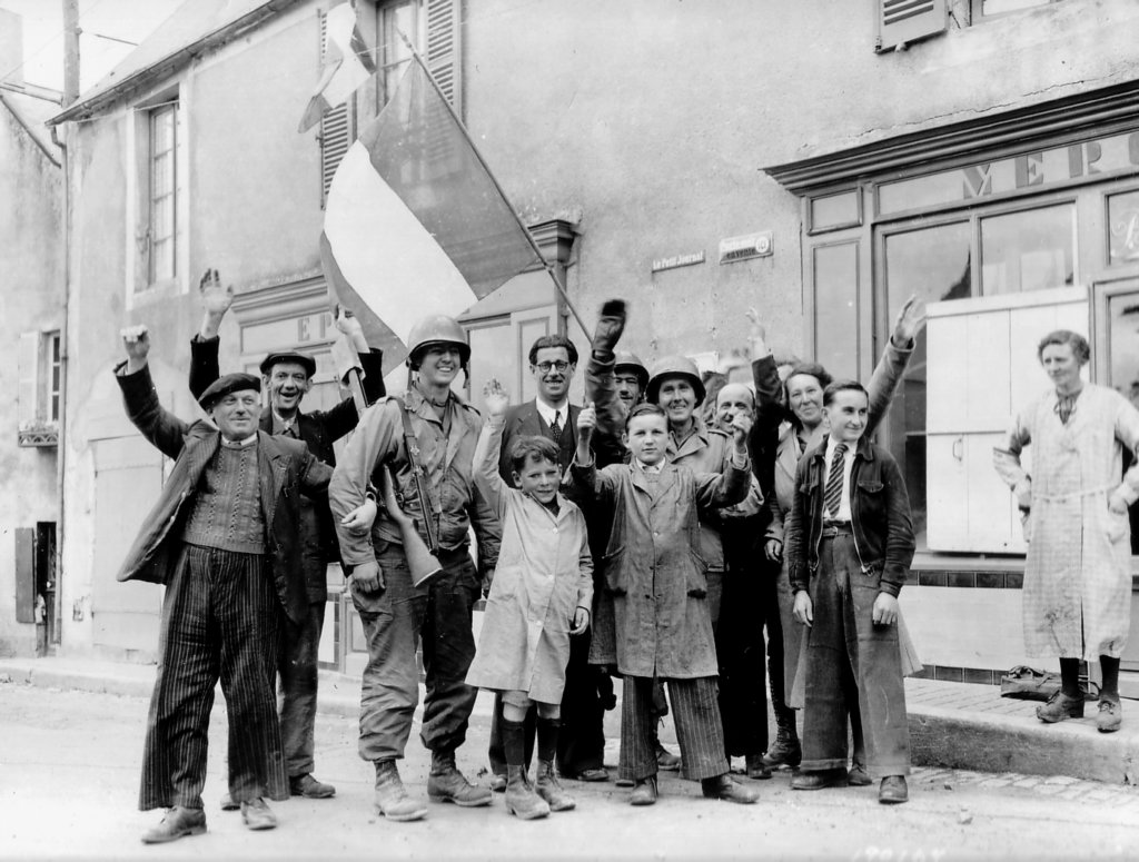 civiliansandtwoussoldierswavingthefrenchflagbeforeahaberdasheryinsaintehonorinedespertes.jpg